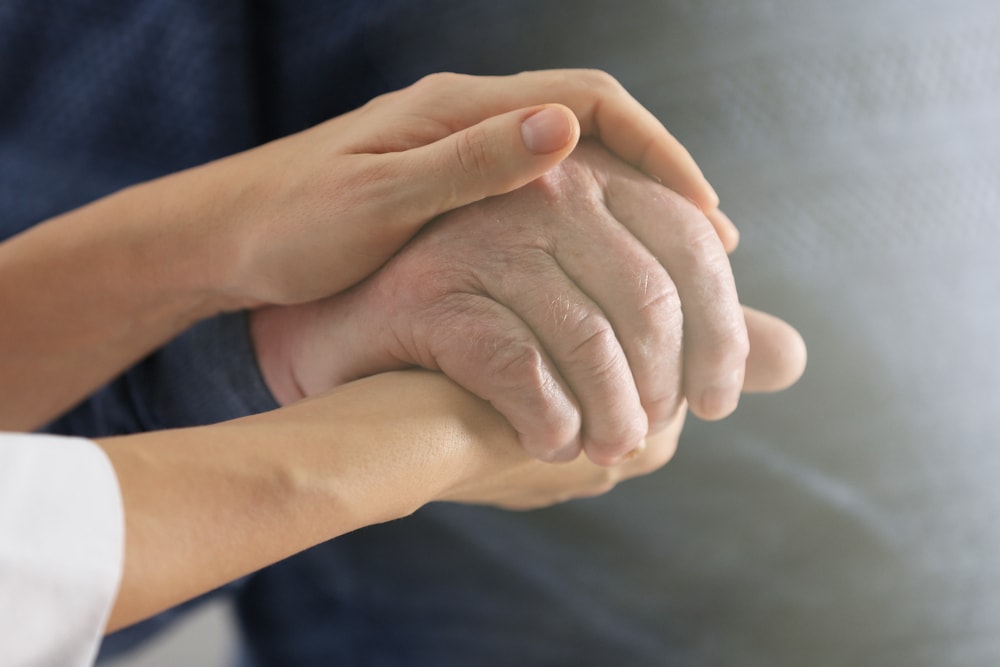 Home health care nurse holding a senior man's hand