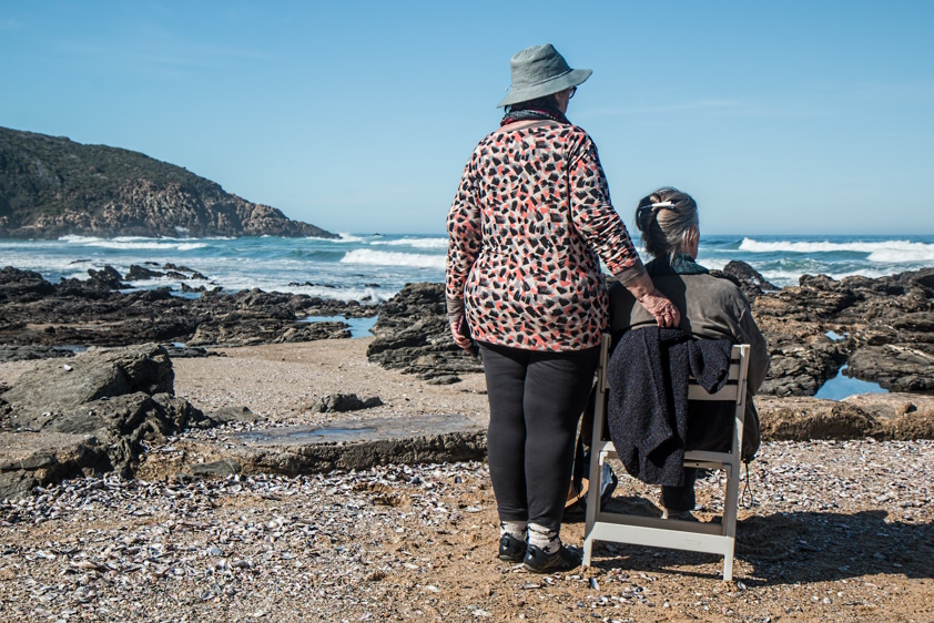 one woman standing with elderly female sitting down looking at the ocean