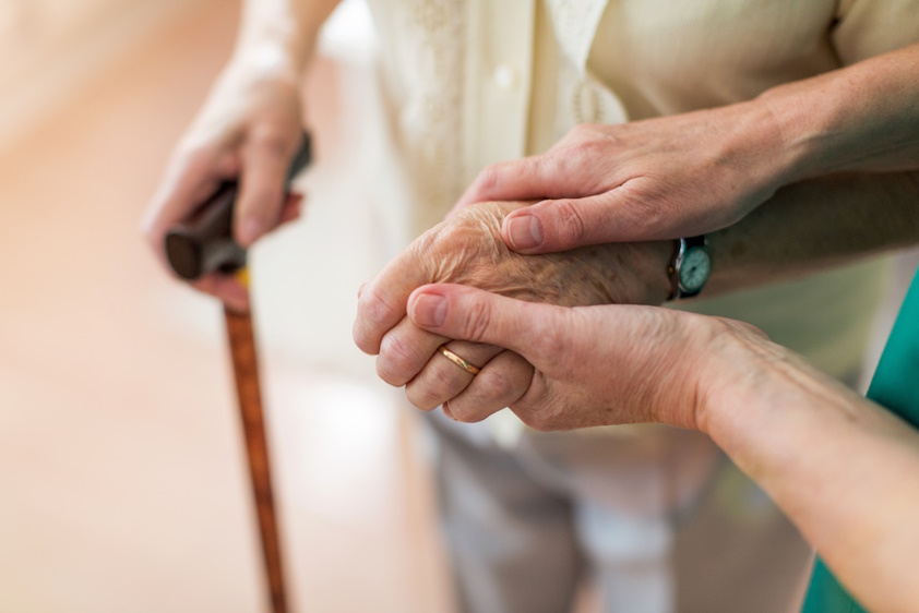 close up of a nurse holding the hand of an older person with a cane