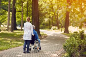hospice nurse pushing man in wheelchair outside