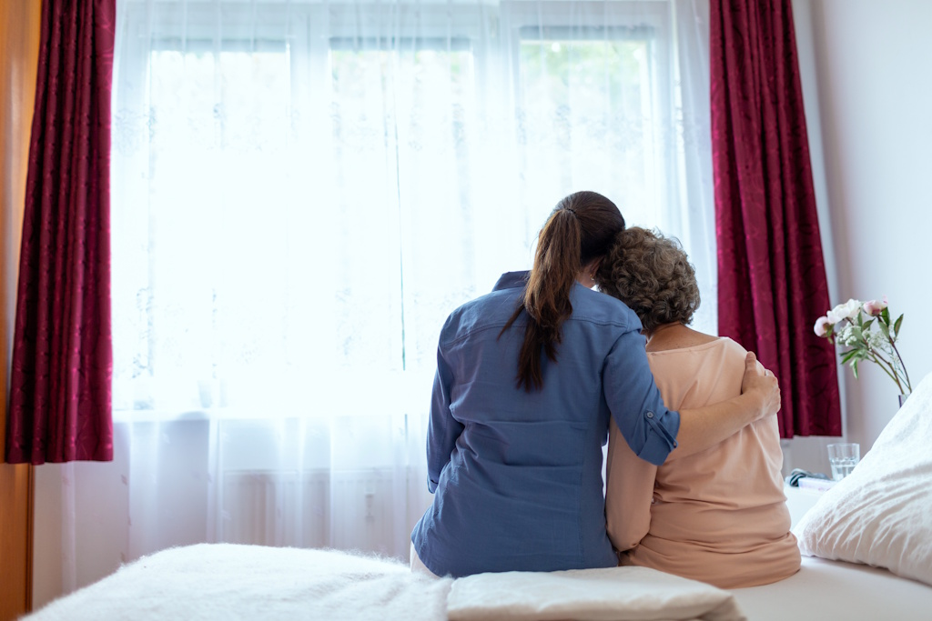 woman hugging senior mother on bed