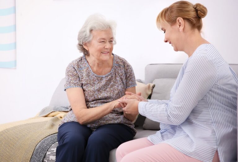 Senior woman and caregiver sitting on sofa at home