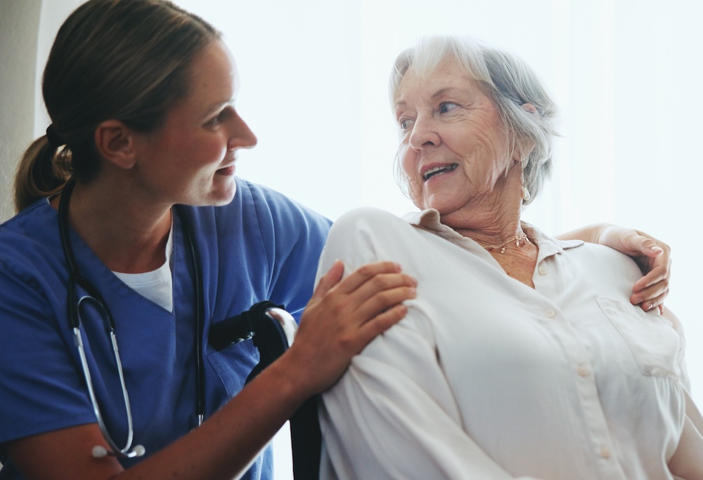 Elderly, woman and nurse for support in wheelchair with assisted living, rehabilitation and happy for assistance. Senior patient, caregiver and smile for wellness, helping hand and healing in hospice